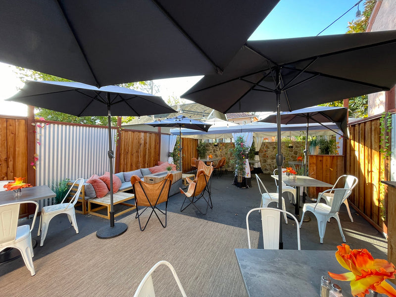 Outdoor restaurant patio with black umbrellas, string lights, and lounge seating along a wood fence