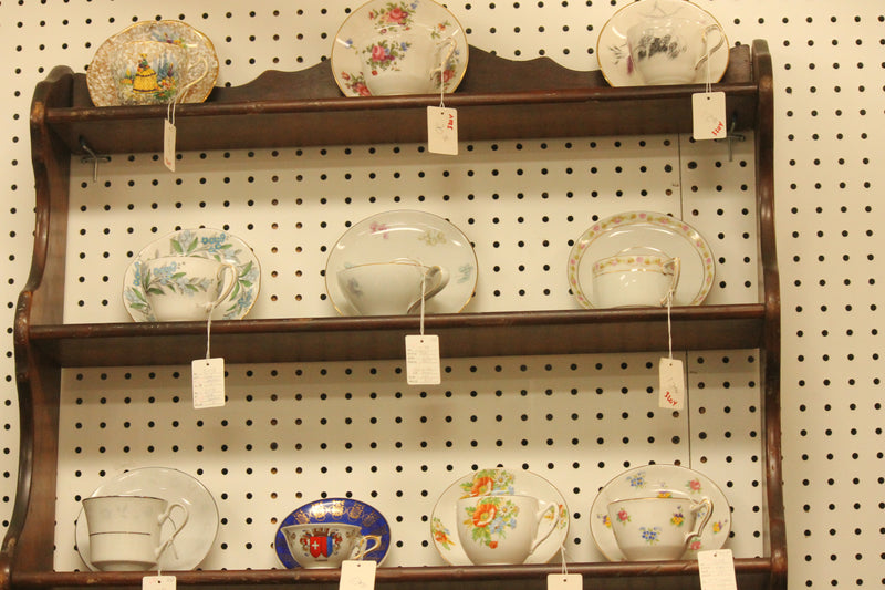 Vintage teacups and saucers with handwritten price tags displayed on an antique wooden shelf